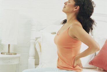 Back pain relief woman sitting on bed with backache.