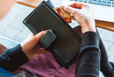 Credit card being inserted into a wallet on a laptop desk.