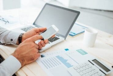 Modern business person using smartphone and laptop for cow trading and market analysis.